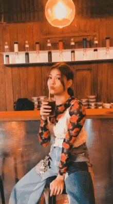 a woman is sitting on a bar stool drinking a beverage through a straw .