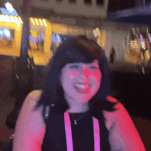 a woman wearing a black top and pink straps is smiling in front of a sign that says ' a ' on it