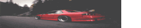 a red car is driving down a road in the dark .