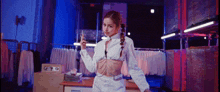 a woman in a white crop top and white pants is standing in a room with clothes .