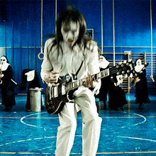 a man with long hair is playing a guitar in front of a group of nuns