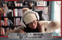 a woman wearing headphones and a beanie is standing in front of a sign that says ' dhani monk '