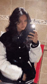 a woman in a black and white jacket is taking a picture of herself in the mirror