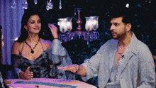a man and woman are sitting at a table with a chandelier in the background