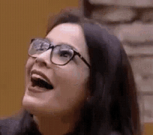 a woman wearing glasses is laughing with her mouth open and looking up .