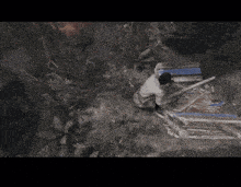 a man in a white shirt is kneeling down in a dark forest