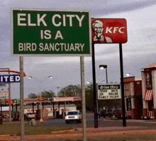 a sign that says elk city is a bird sanctuary next to a kfc sign
