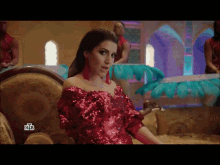 a woman in a red sequined dress is sitting on a couch in front of a sign that says nb