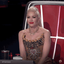 a woman in a gold dress sits in front of a nbc monitor
