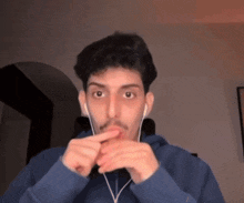 a man wearing ear buds and a blue hoodie looks at the camera