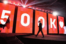 a man walking on a stage in front of a large screen that says 500k