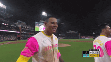 a man in a pink and yellow jersey stands on a baseball field in front of a sign that says petco