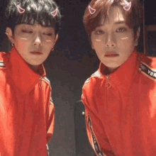 two young men wearing red jackets are standing next to each other and looking at themselves in a mirror .