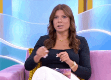 a woman in a black shirt is sitting on a pink couch talking
