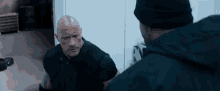 two men are standing next to each other in a room and talking .