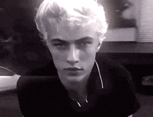 a black and white photo of a young man with blonde hair and a black shirt .