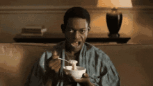 a man is sitting on a couch eating cereal with a spoon .
