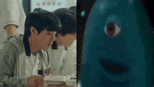 a man is sitting at a table with a spoon in his hand next to a blue monster .