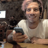 a man with pink hair is smiling while holding a cellphone