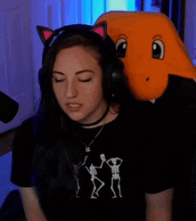 a woman wearing headphones and a black shirt with skeletons on it is sitting in front of an orange stuffed animal .