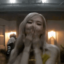a woman with blonde hair is covering her mouth with her hands while wearing a black shirt with the word three on it