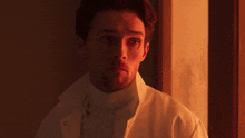 a man wearing a white coat and a turtleneck looks at the camera