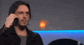 a man in a black jacket is talking on a cell phone with an abc logo in the corner