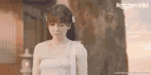a woman in a white dress is standing in front of a tree and looking down .