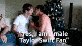two men kissing in front of a christmas tree with the words " yes i am a male taylor swift fan " below them