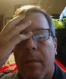a man wearing glasses is rubbing his forehead with his hand