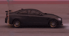 a black sports car with gold wheels is driving on a race track .