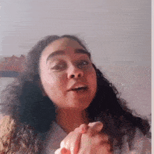 a woman with curly hair is making a funny face while holding her hands together in front of her face .