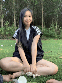 a girl is sitting on the grass with her legs crossed and smiling