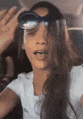 a woman wearing sunglasses and a white t-shirt is making a funny face .