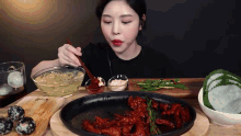 a woman in a black shirt is eating a plate of food with a bowl of noodles on the table