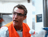 a man wearing safety glasses and an orange vest is holding a spray bottle .