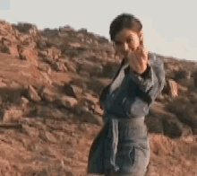 a woman in a denim jacket is giving the middle finger in front of a mountain
