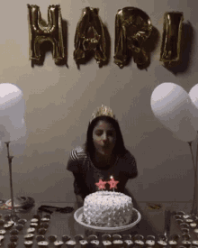 a woman blowing out candles on a cake with the word hari balloons behind her