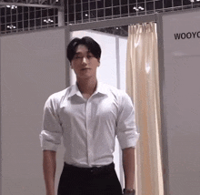 a man in a white shirt and black pants is standing in a room with a sign that says woo