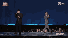 two men singing on a stage with a banner that says mnet