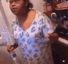 a woman is standing in a kitchen holding a water bottle .