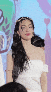 a woman in a white dress with a crown on her head is looking at the camera