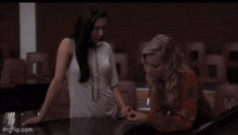 two women are standing next to each other at a table in a classroom .