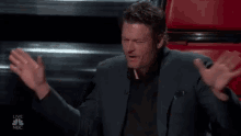 a man in a suit is making a heart shape with his hands while sitting on a stage .
