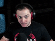 a man wearing headphones and a black shirt is sitting in front of a microphone .