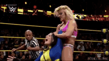 two women are wrestling in a ring with a referee watching