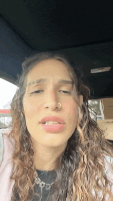 a woman with curly hair and a nose ring looks at the camera