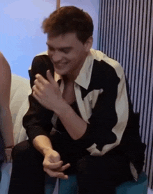 a man in a black and white shirt is sitting on a couch laughing .