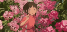 a girl in a red shirt is standing in a garden of pink flowers .