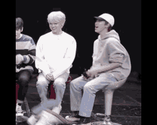 a group of young men are sitting on stools and one of them is wearing a white hat
